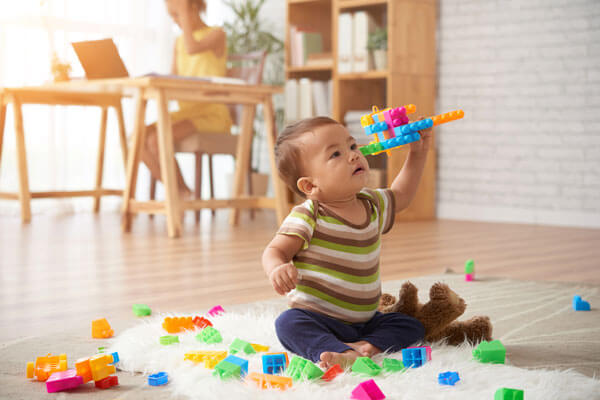Advizi - La photo représente un bébé assis qui fait voler un avion en lego multicolore.